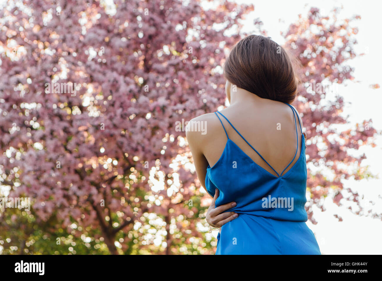 Back view of a beautiful young woman dressed in blue overalls standing ...