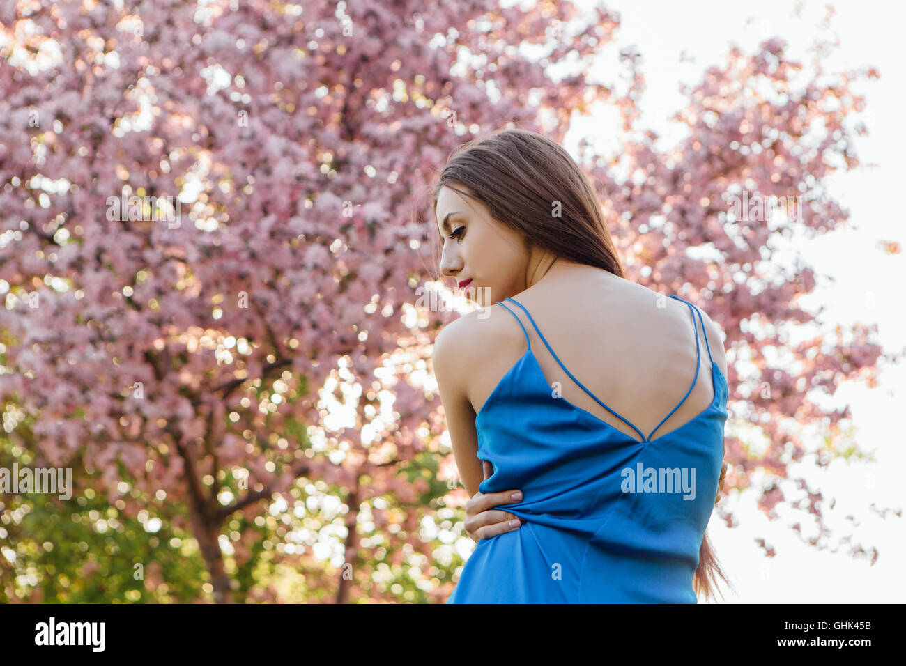 Back view of a beautiful young woman dressed in blue overalls standing ...