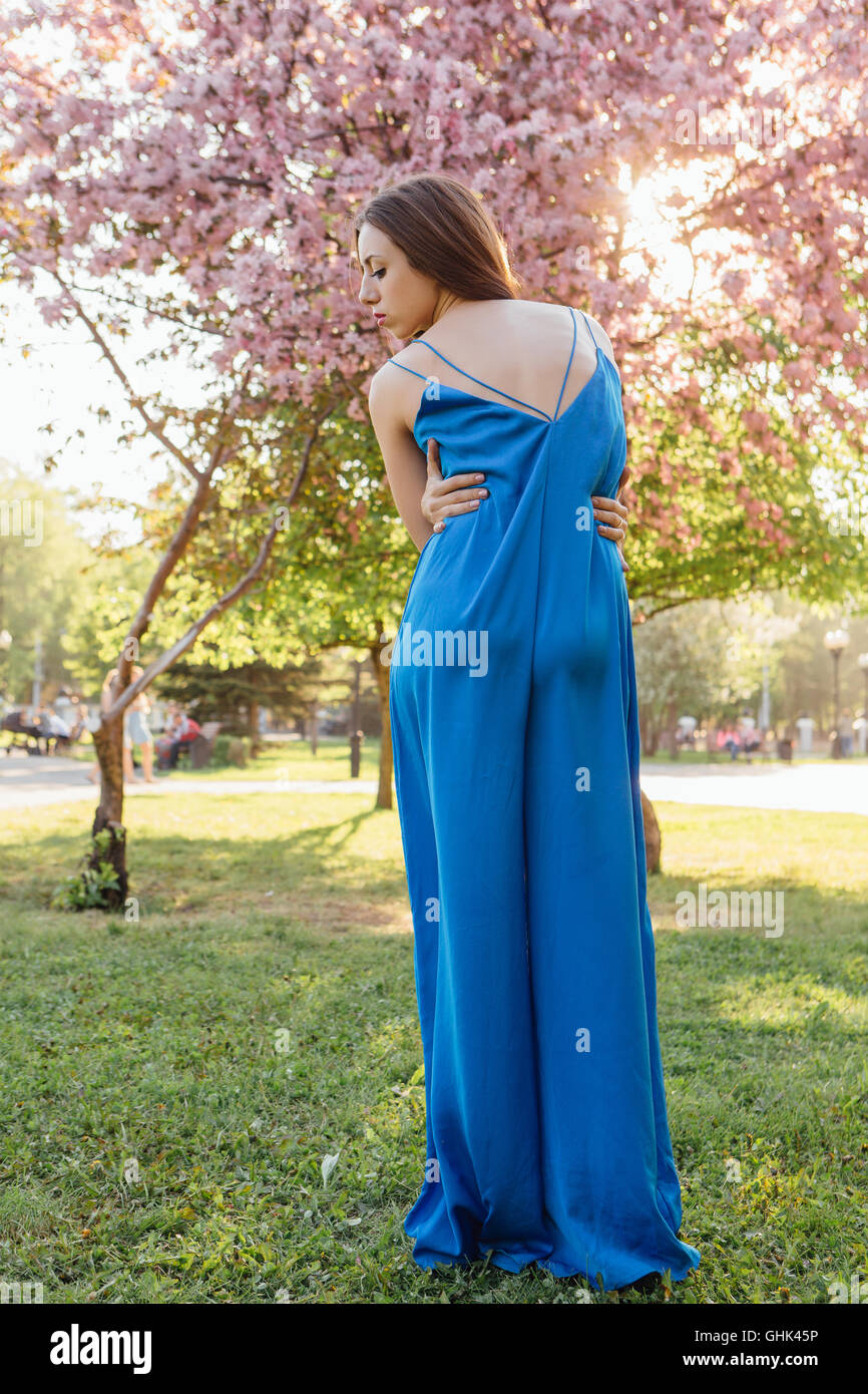 Back view of a beautiful young woman dressed in blue overalls standing ...