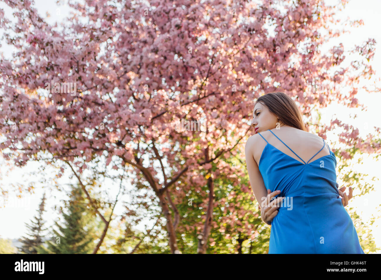 Back view of a beautiful young woman dressed in blue overalls standing ...