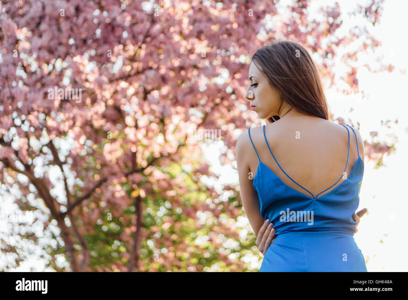 Back view of a beautiful young woman dressed in blue overalls standing ...