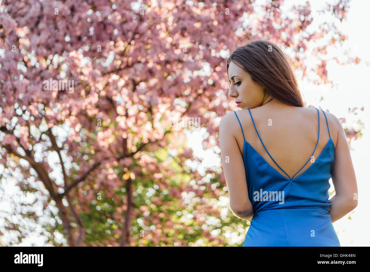 Back view of a beautiful young woman dressed in blue overalls standing ...