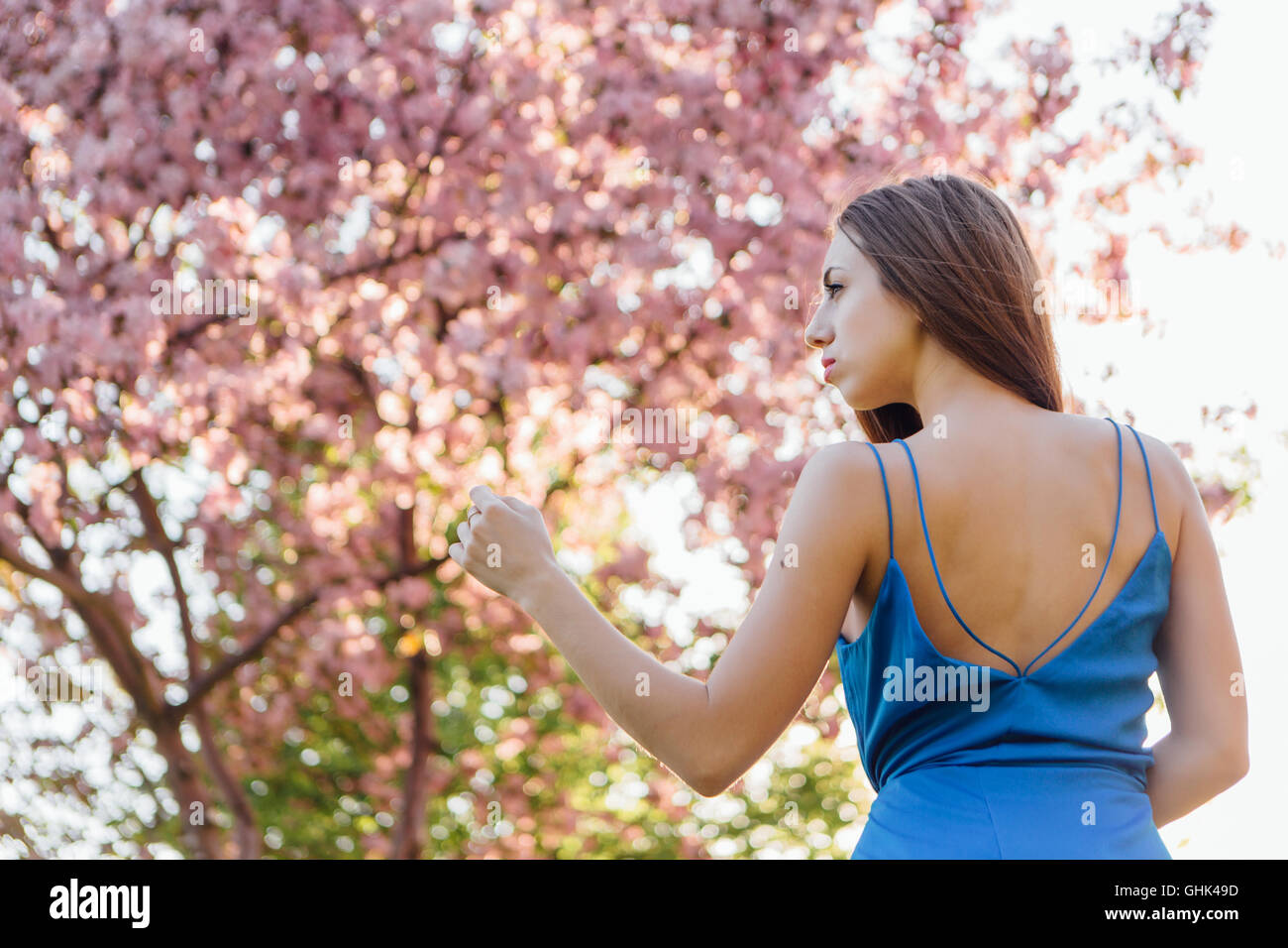 Back view of a beautiful young woman dressed in blue overalls standing ...