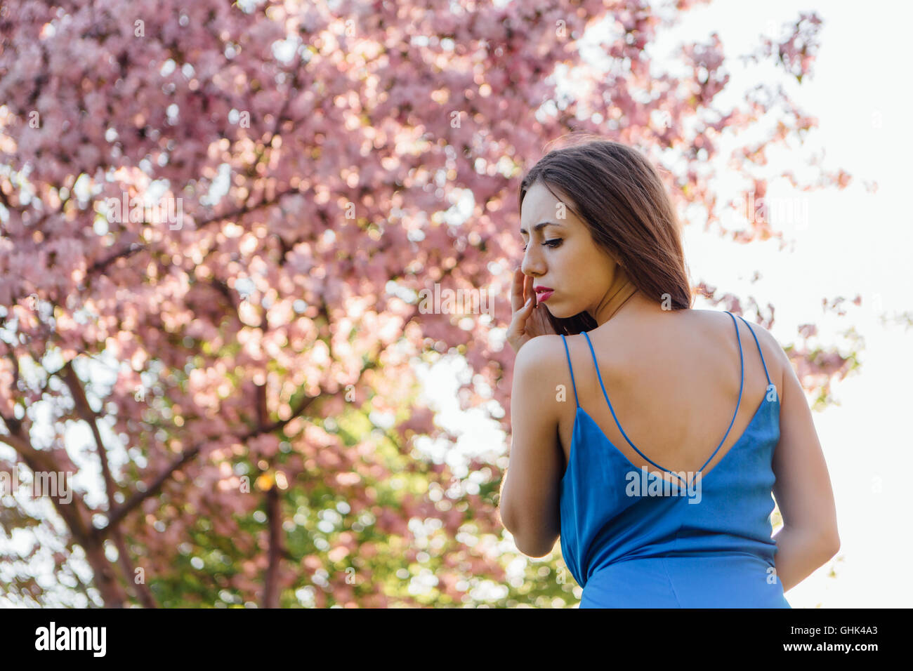 Back view of a beautiful young woman dressed in blue overalls standing ...