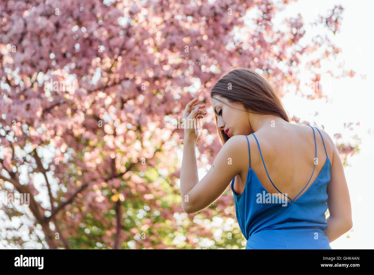 Back view of a beautiful young woman dressed in blue overalls standing ...