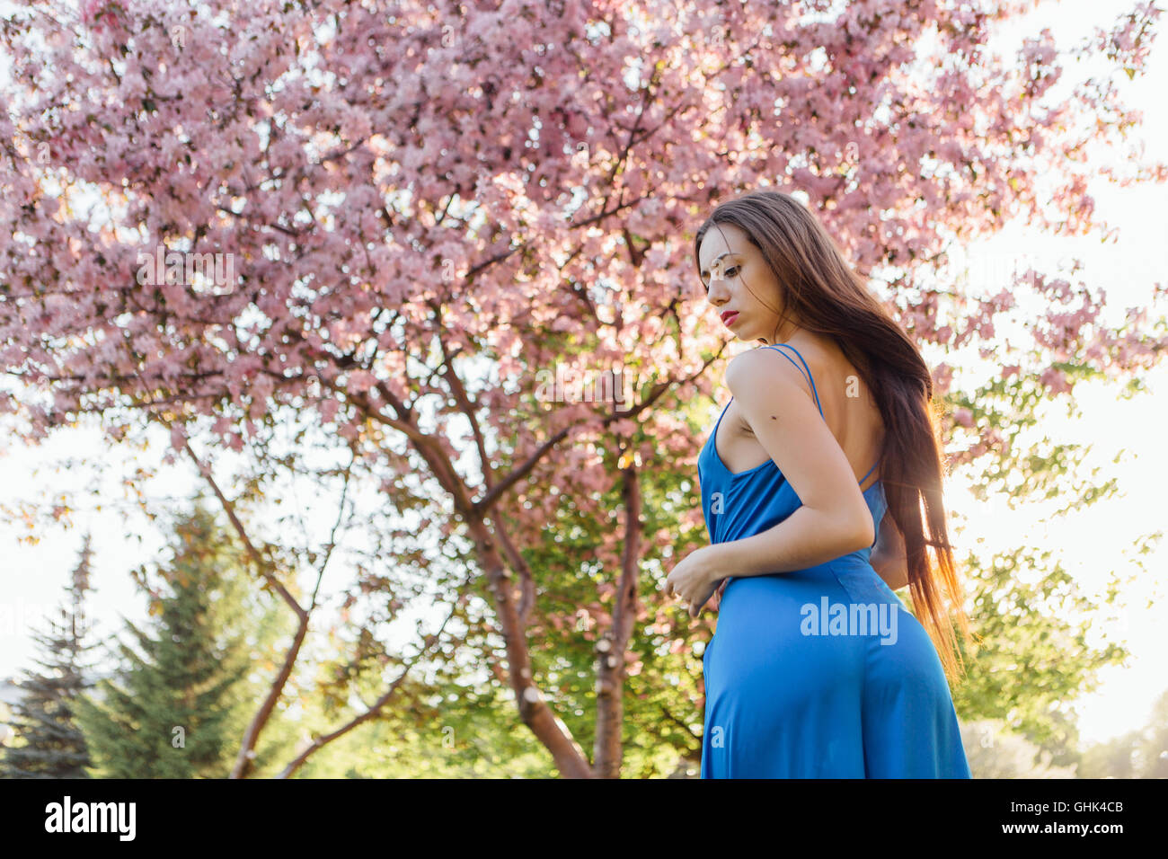 Back view of a beautiful young woman dressed in blue overalls standing ...