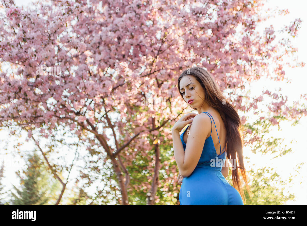 Back view of a beautiful young woman dressed in blue overalls standing ...