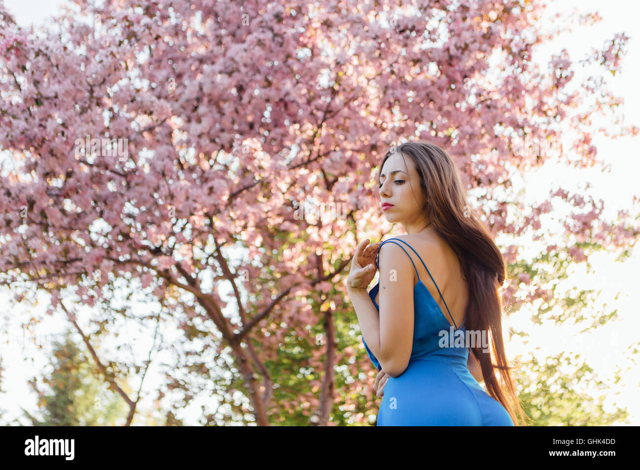 Back view of a beautiful young woman dressed in blue overalls standing ...