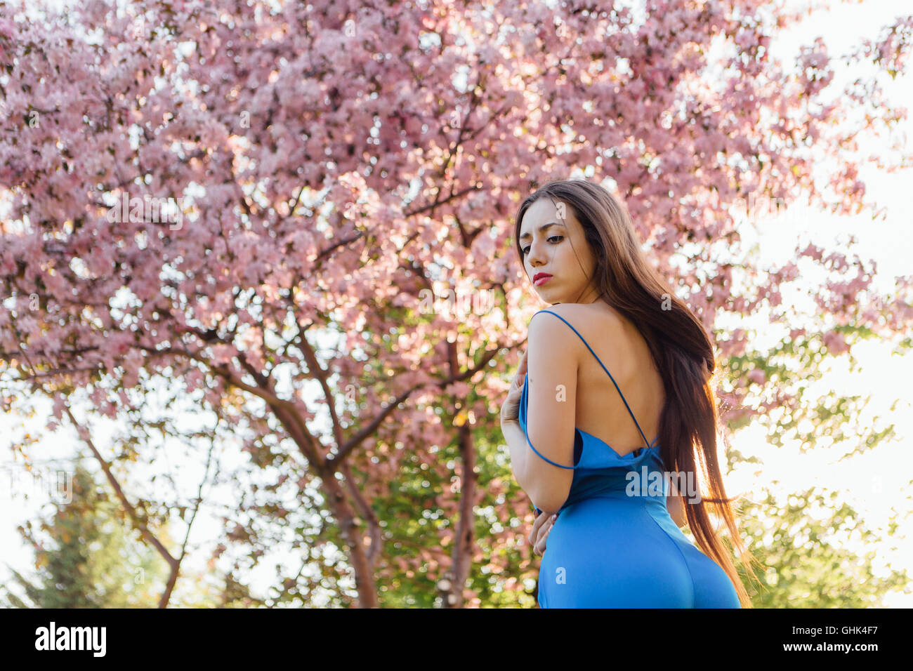 Back view of a beautiful young woman dressed in blue overalls standing ...