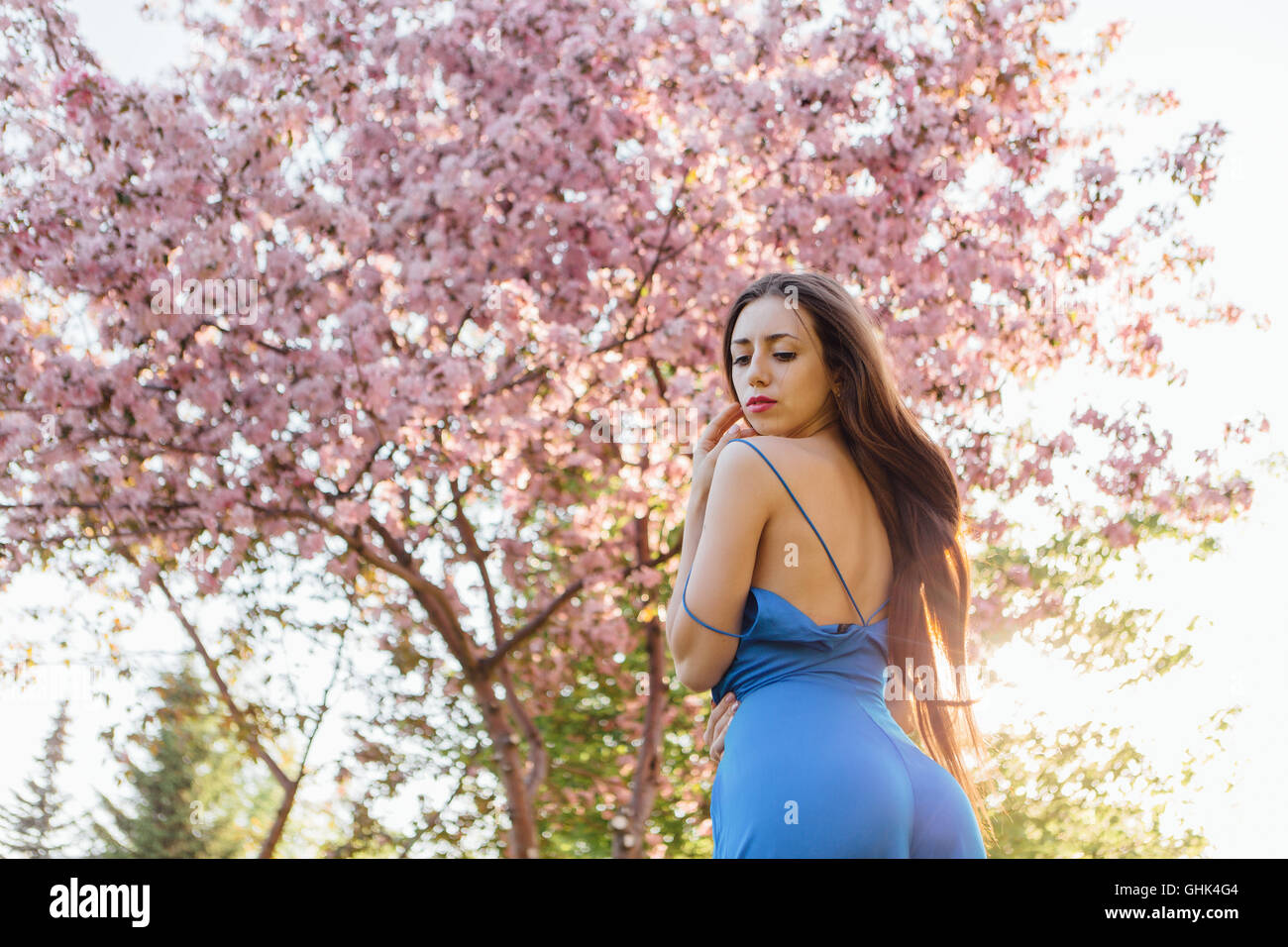 Back view of a beautiful young woman dressed in blue overalls standing ...