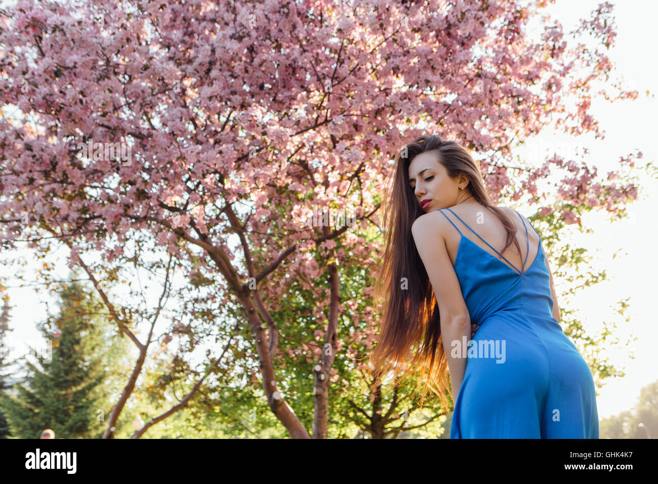 Back view of a beautiful young woman dressed in blue overalls standing ...