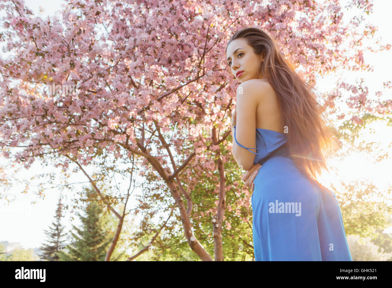Back view of a beautiful young woman dressed in blue overalls standing ...