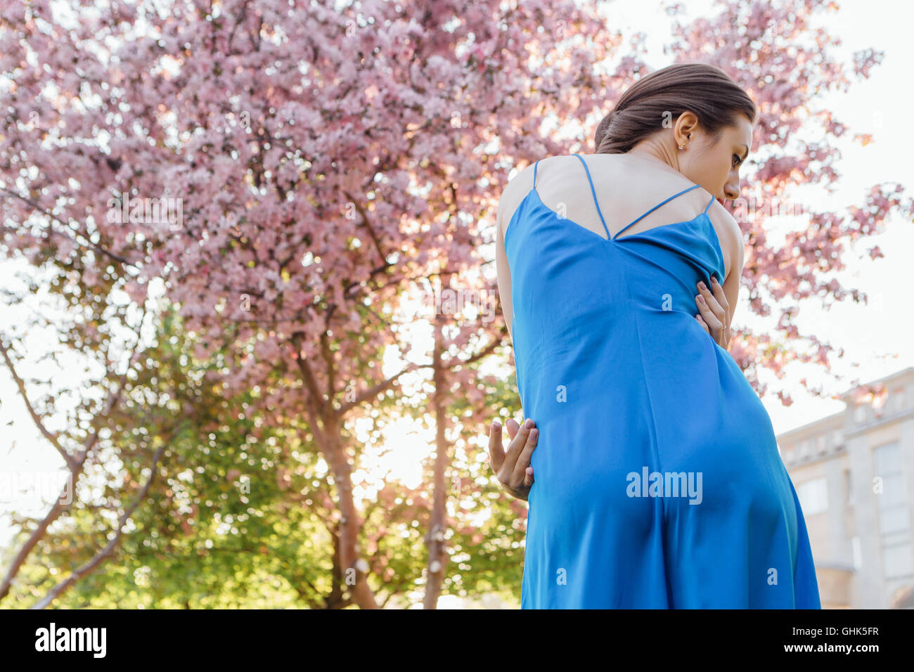 Back view of a beautiful young woman dressed in blue overalls standing ...