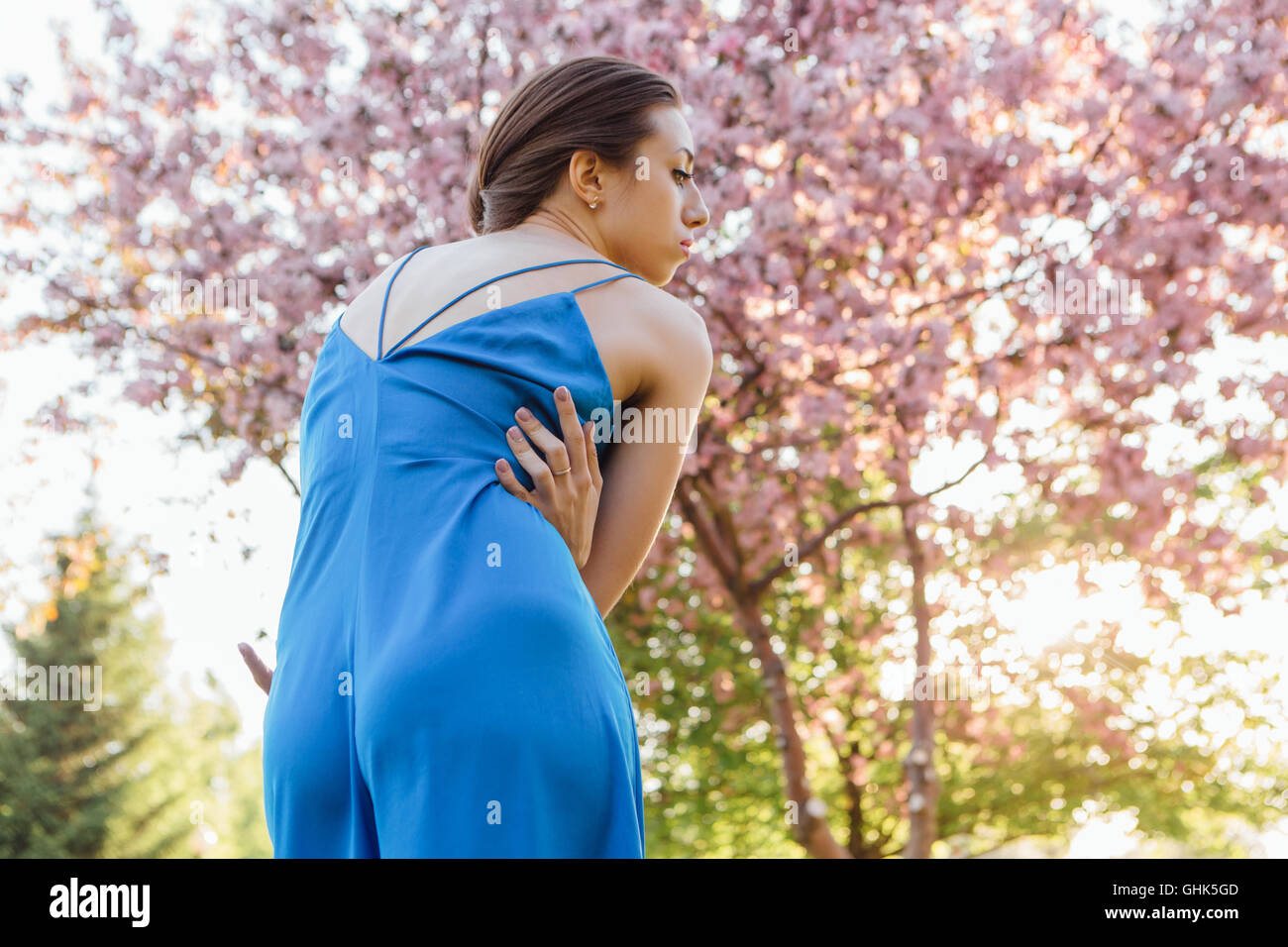 Back view of a beautiful young woman dressed in blue overalls standing ...
