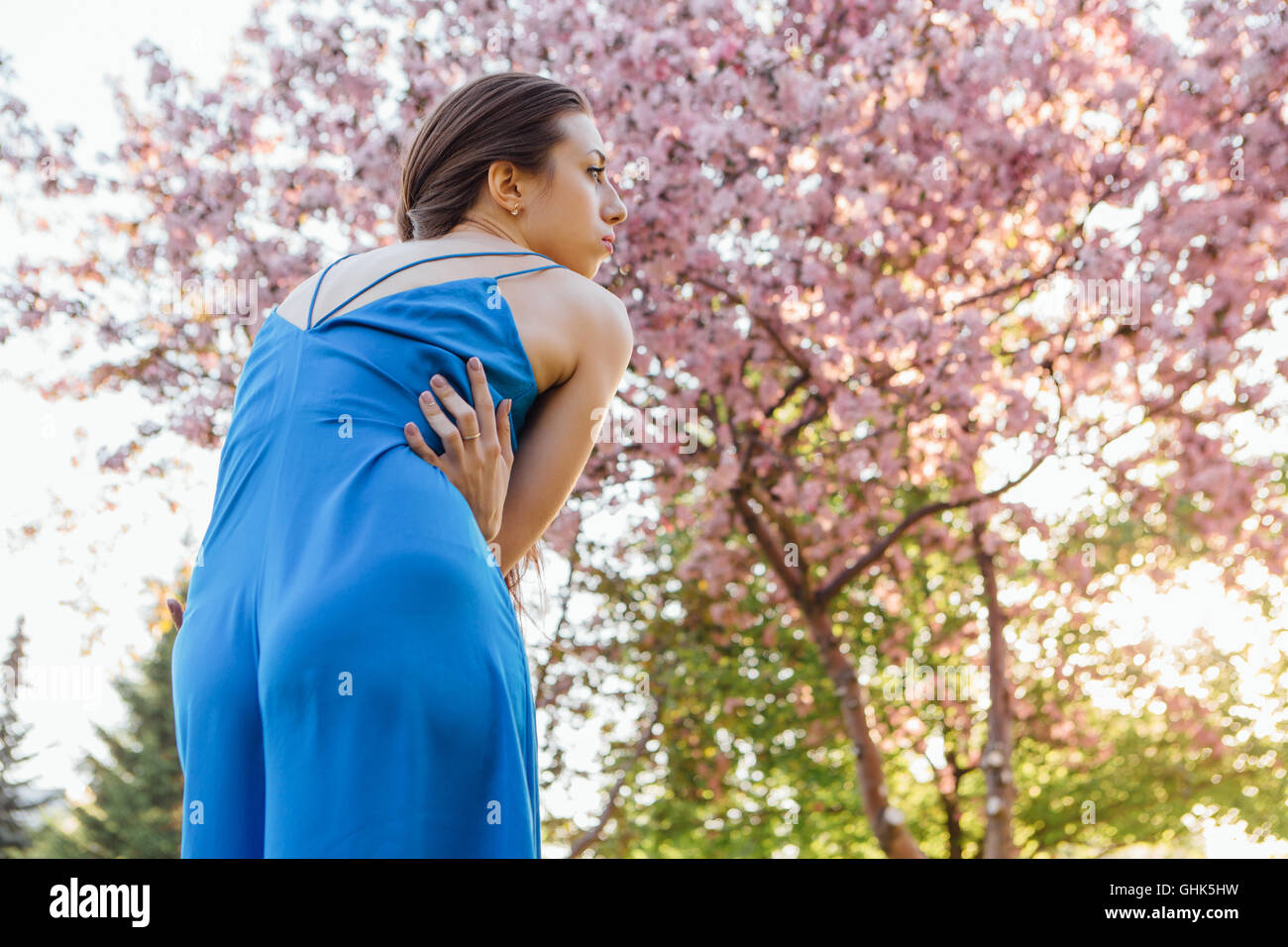 Back view of a beautiful young woman dressed in blue overalls standing ...