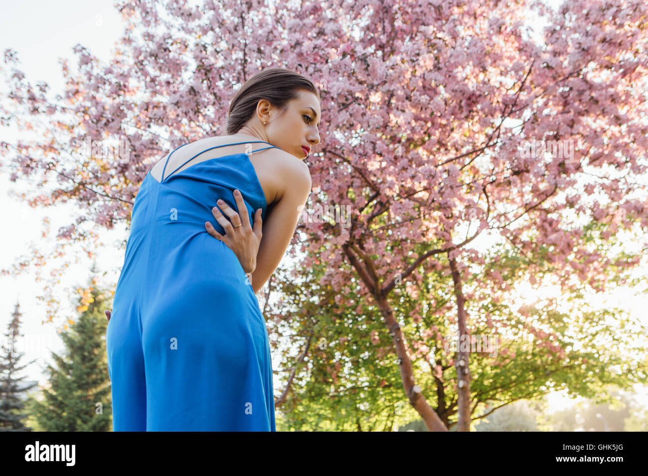 Back view of a beautiful young woman dressed in blue overalls standing ...