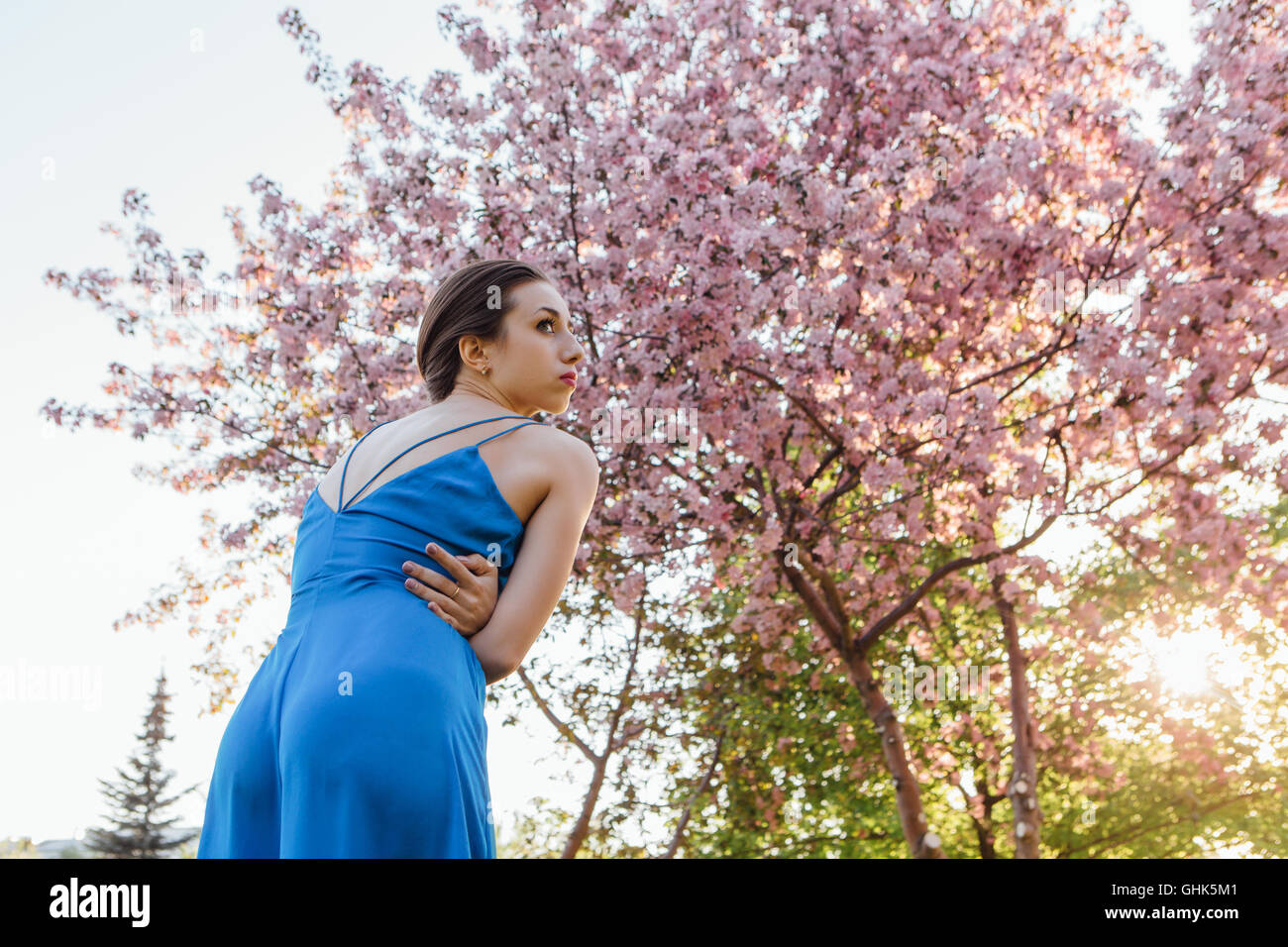 Back view of a beautiful young woman dressed in blue overalls standing ...