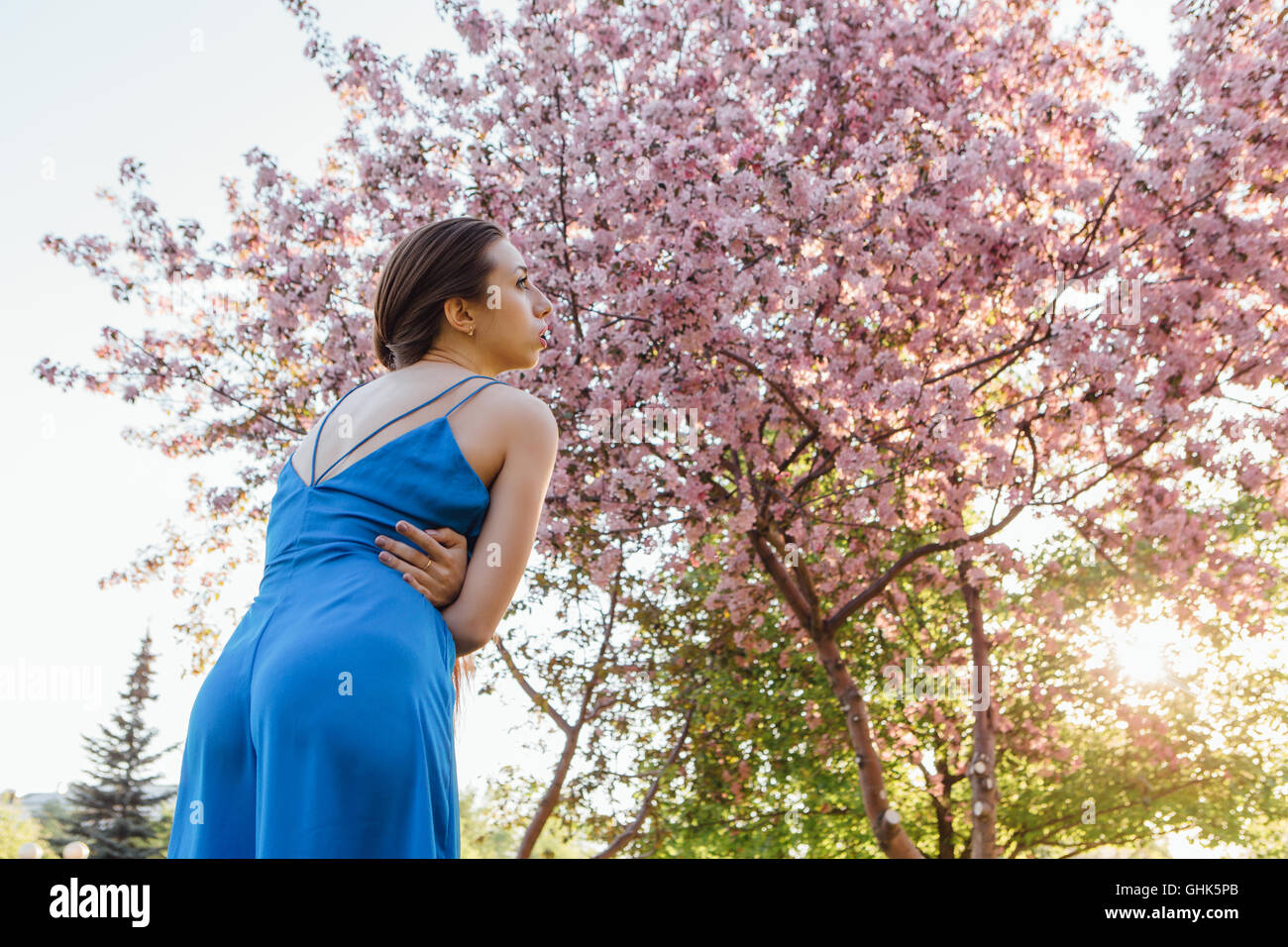 Back view of a beautiful young woman dressed in blue overalls standing ...