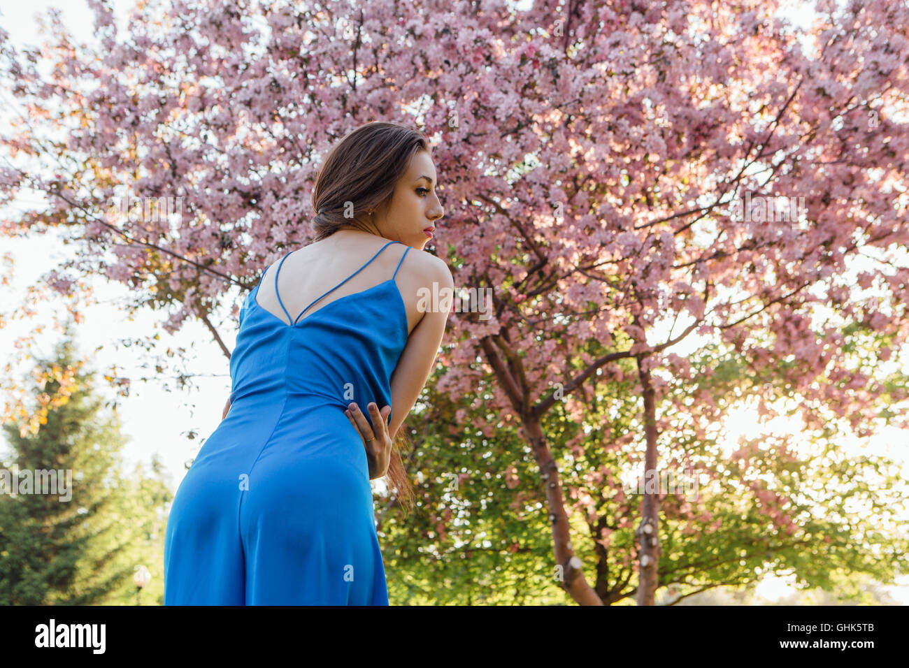 Back view of a beautiful young woman dressed in blue overalls standing ...