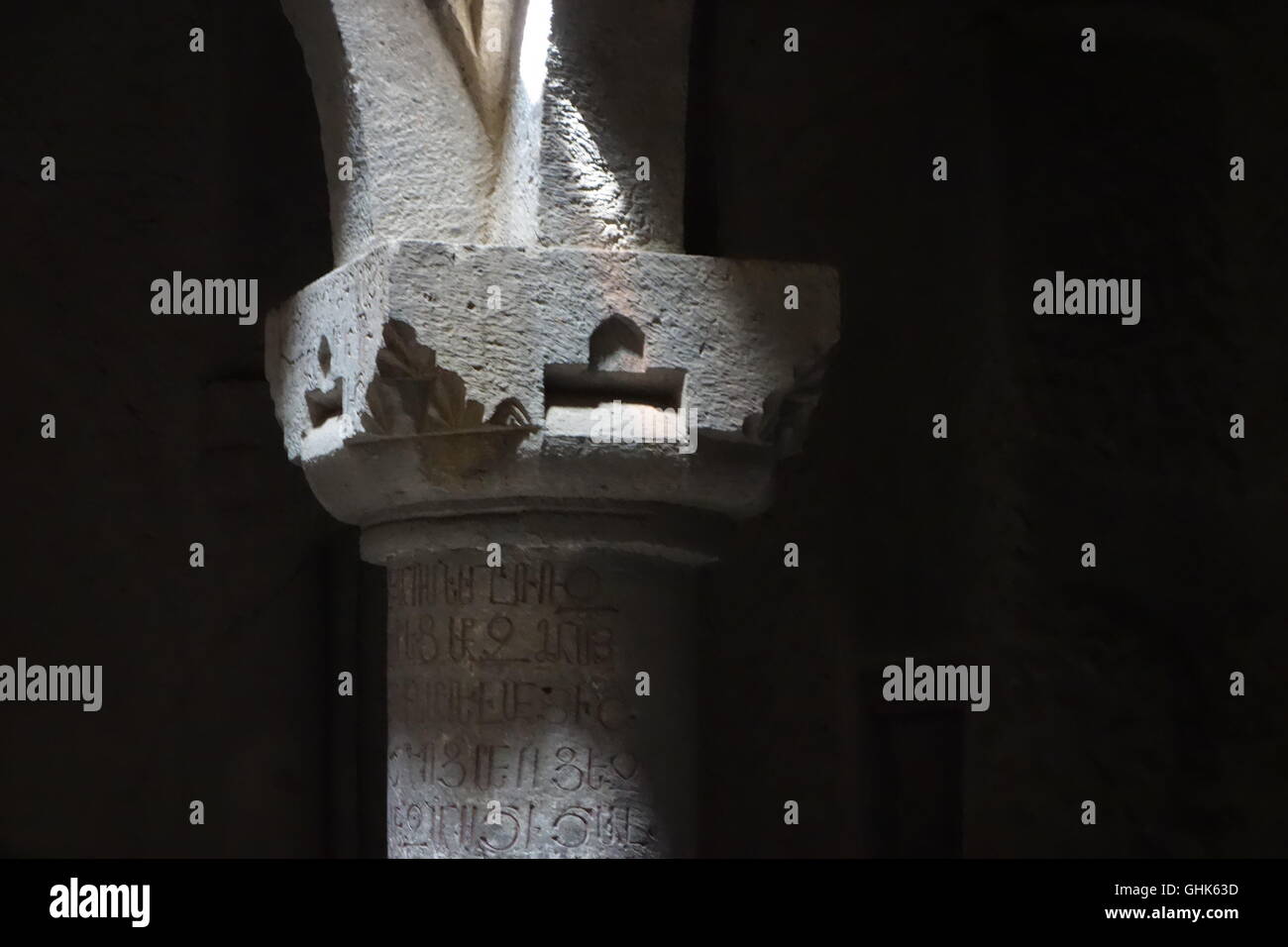 Geghard Armenia cave cut church simple capital with oriental type motif basalt Armenian script on column below UNESCO site Stock Photo