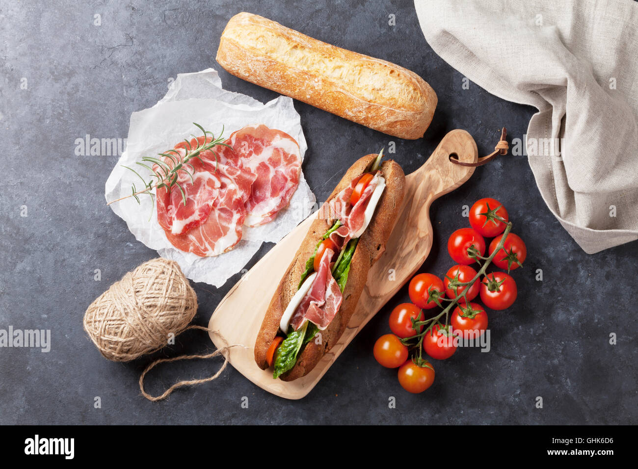 Ciabatta sandwich with romaine salad, prosciutto and mozzarella cheese over stone background
