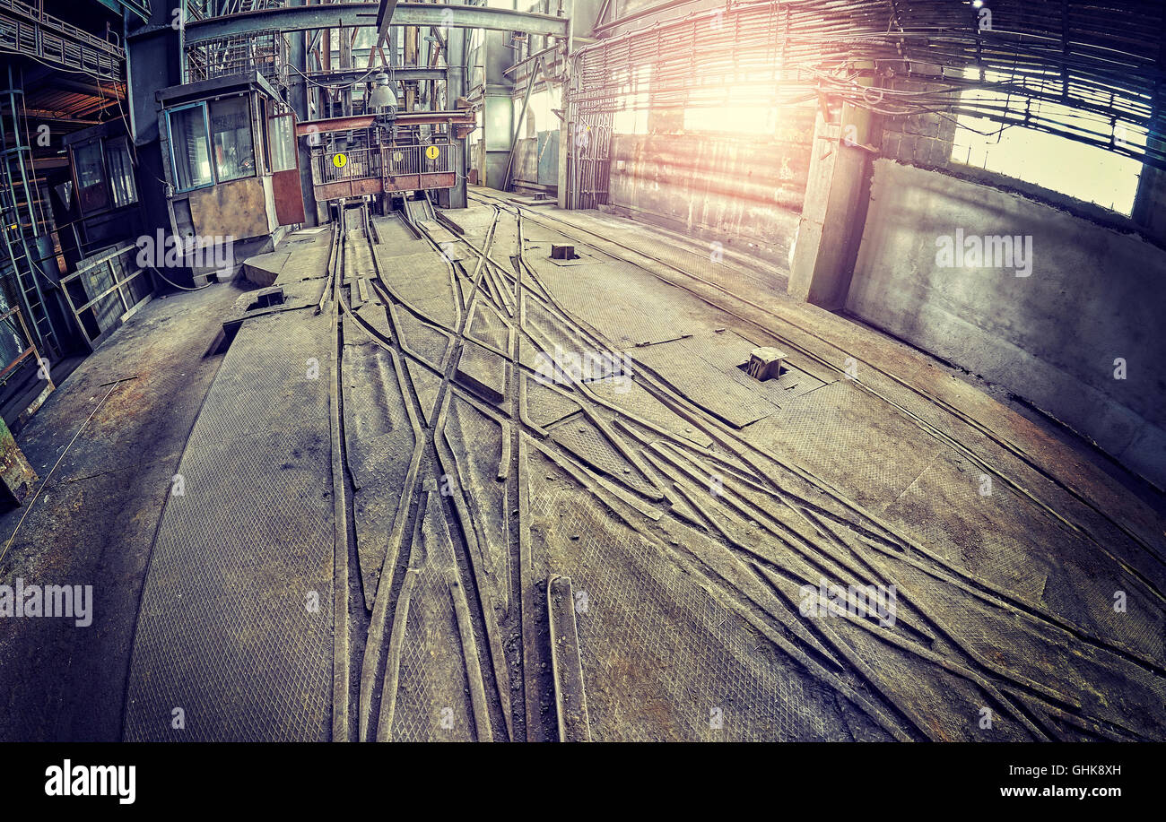 Vintage toned fisheye lens picture of abandoned industrial hall interior with trolley tracks. Stock Photo