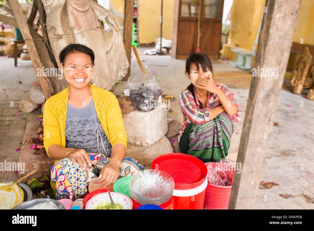 Burmese woman with beaming smile, preparing food while daughter watches on, Mandalay Myanmar. Stock Photo