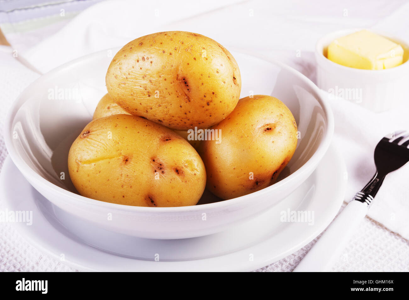 Boiled jacket potatoes served in a white bowl with butter Stock Photo