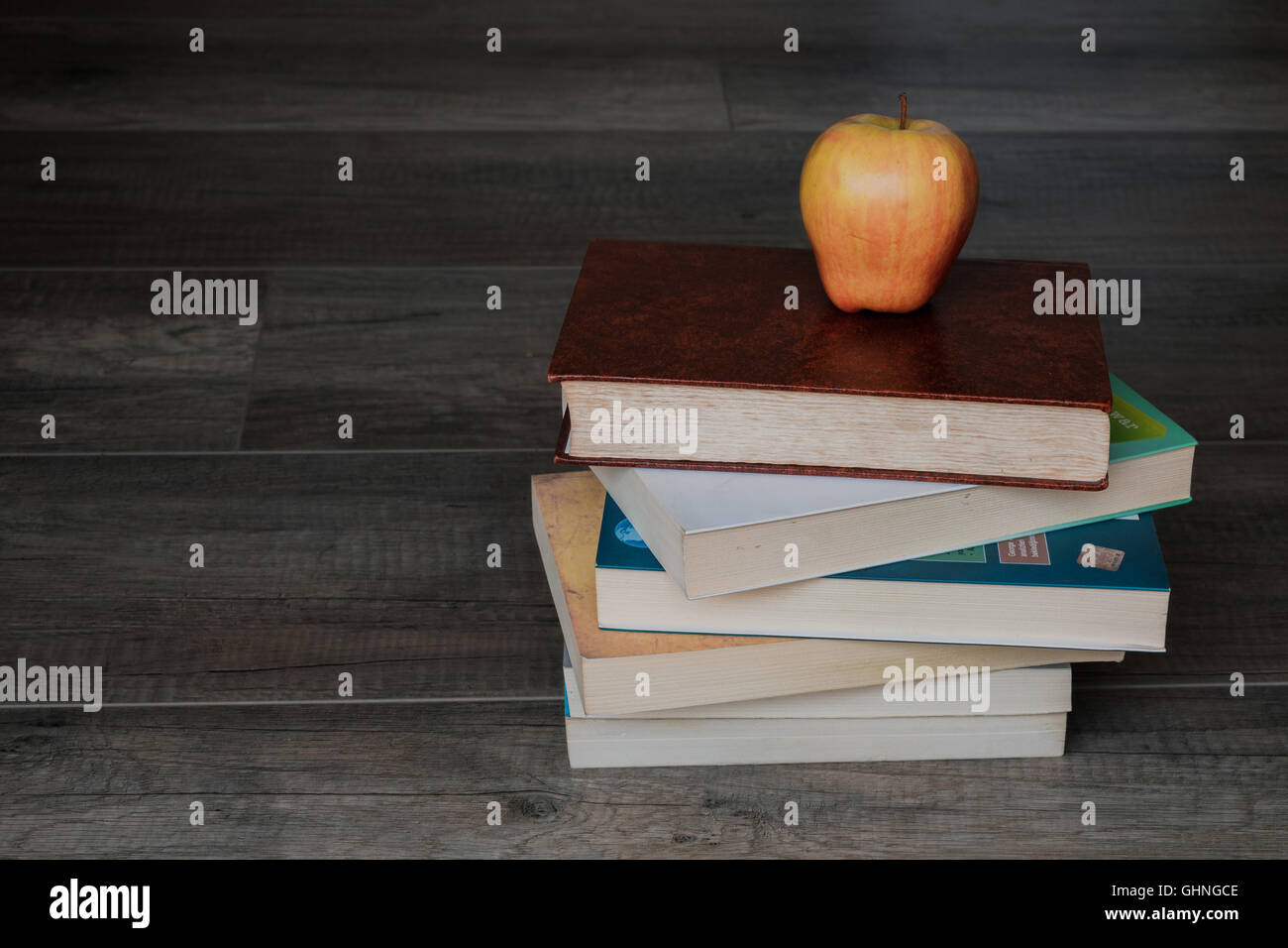 A pile of books with an apple on top on the wooden background Stock Photo