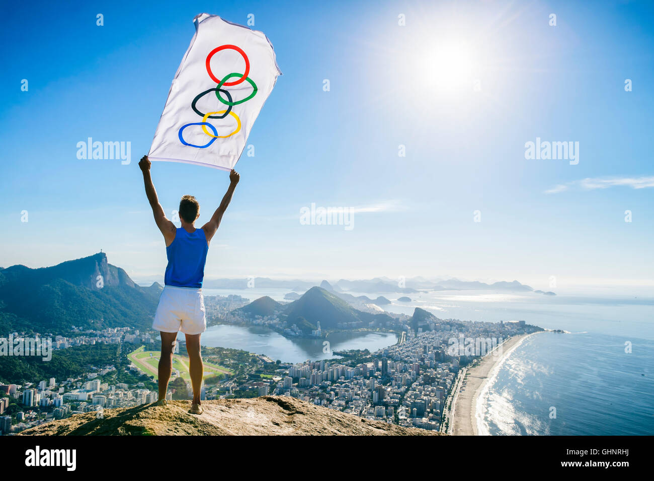 RIO DE JANEIRO - MARCH 21, 2016: Athlete stands holding Olympic flag above a city skyline view of Corcovado and Zona Sul. Stock Photo