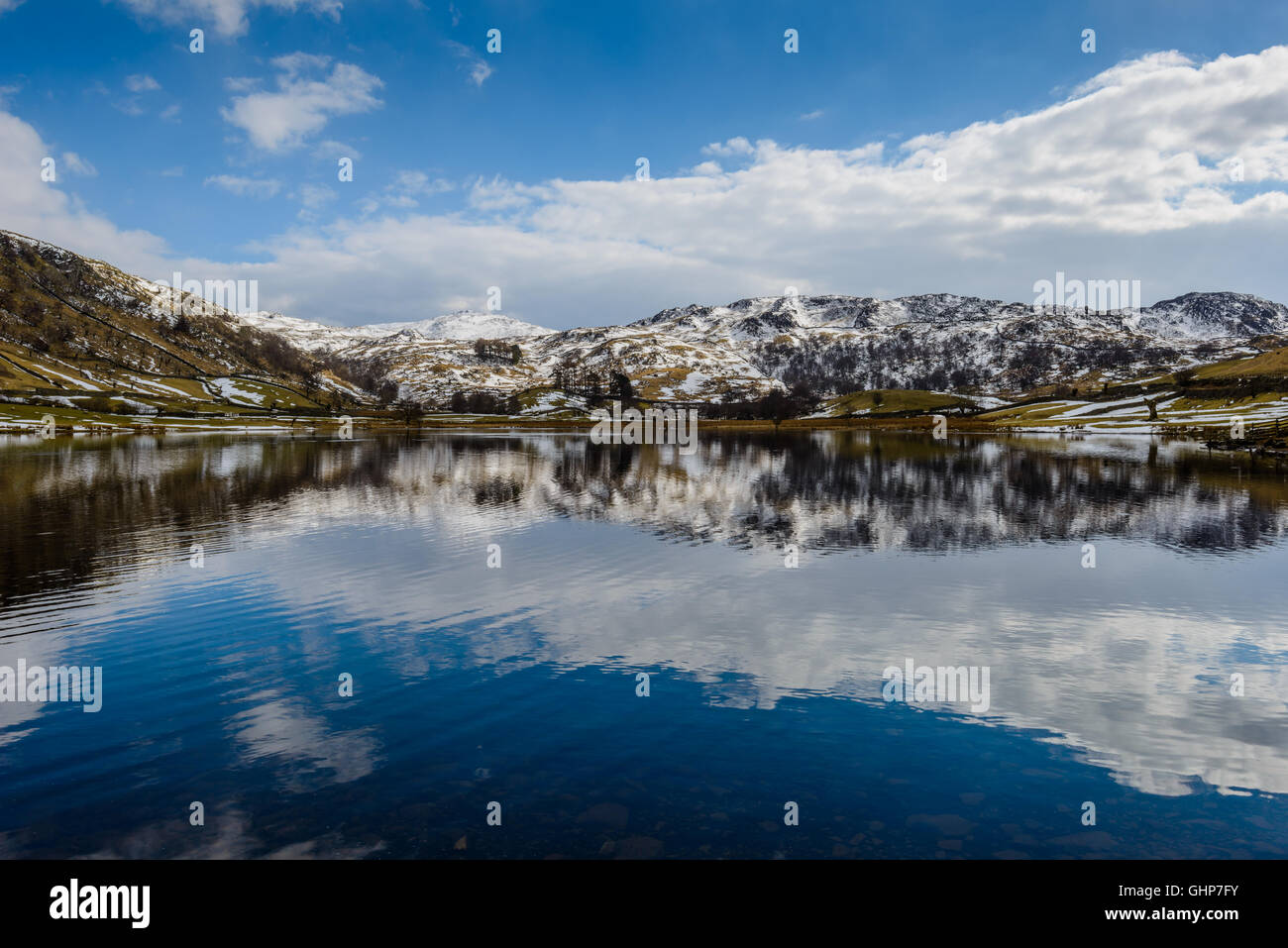 Watendlath tarn in the Lake District surrounded by snow capped fells on a late March afternoon. Stock Photo