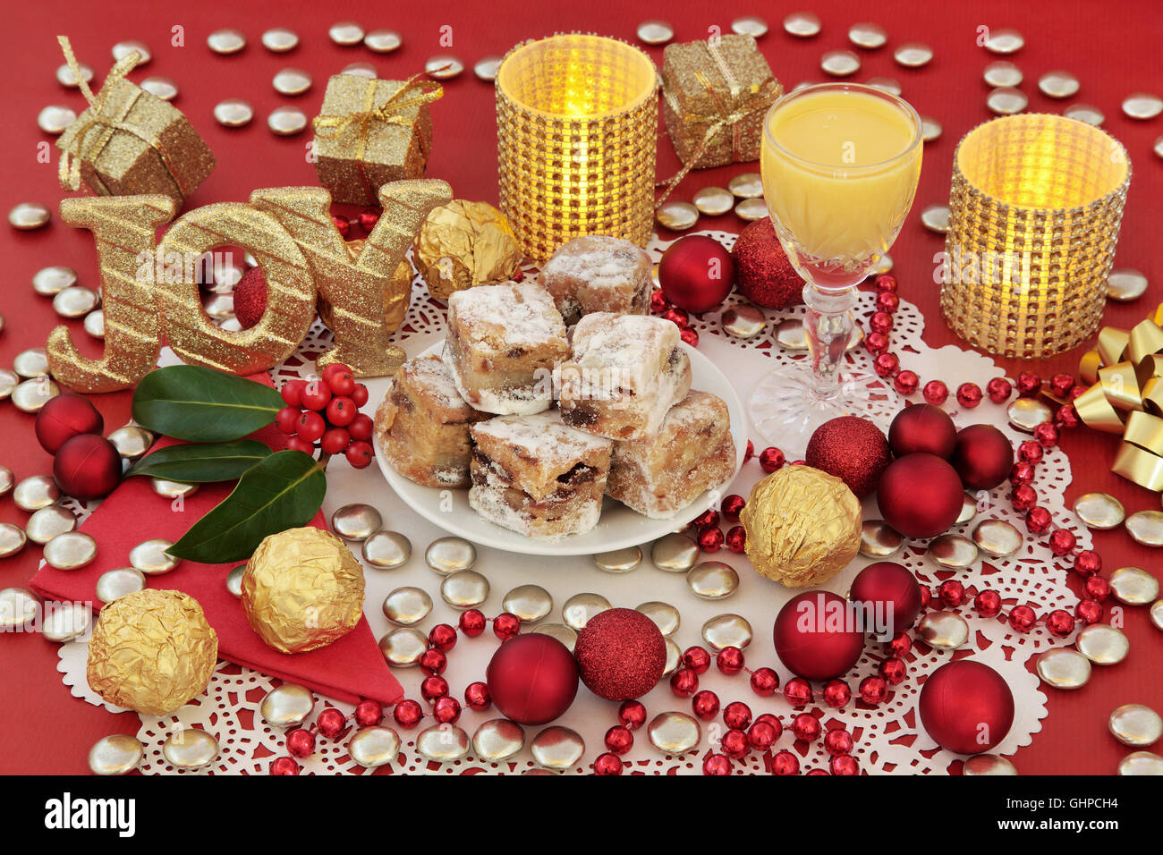 Christmas sweet food with stollen cake bites, candles, gold glitter joy sign, advocaat egg nog, holly and decorations. Stock Photo