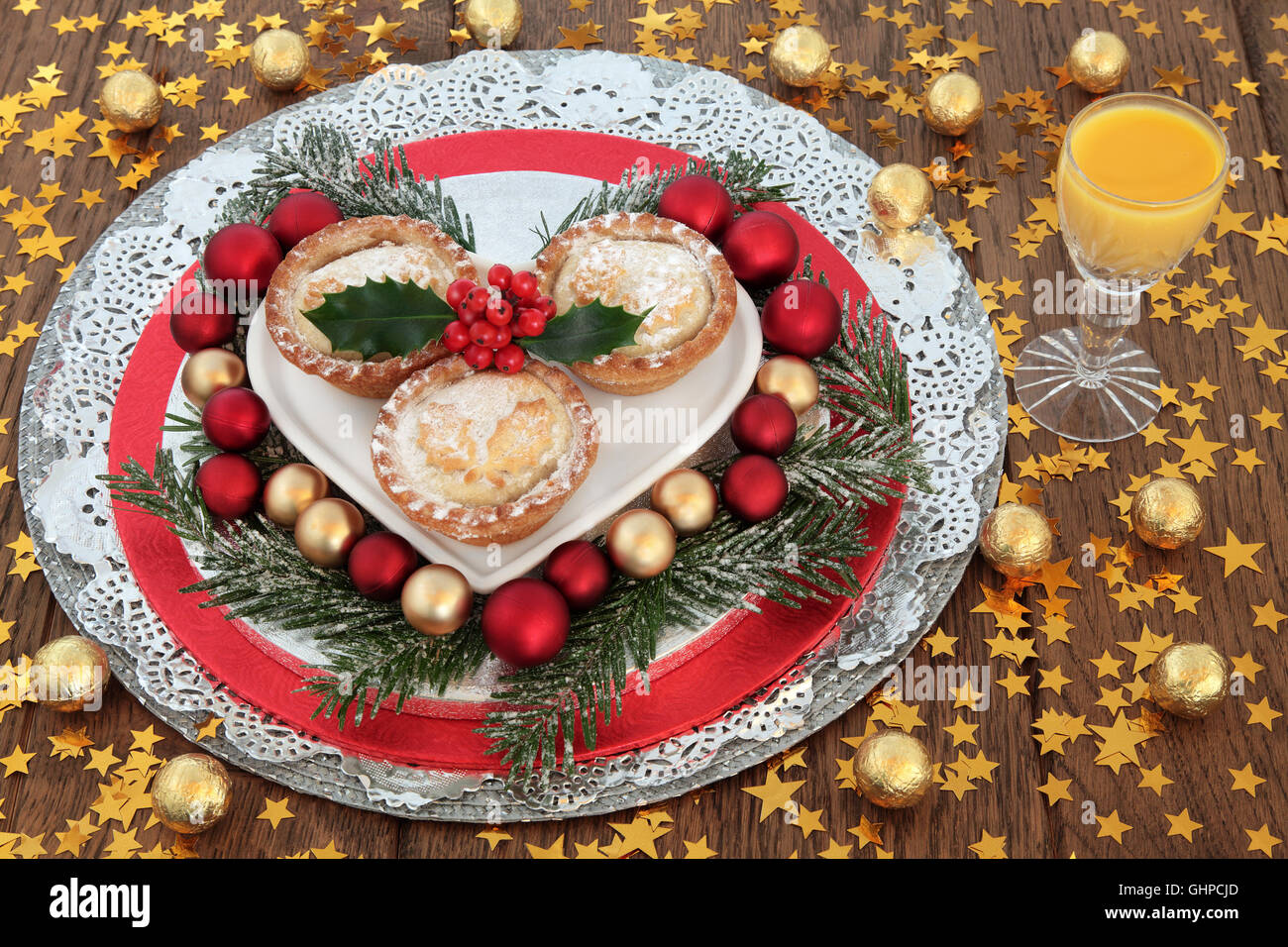 Christmas egg nog, mince pies with holly, snow covered fir, red and gold baubles, foil wrapped chocolate balls and stars. Stock Photo