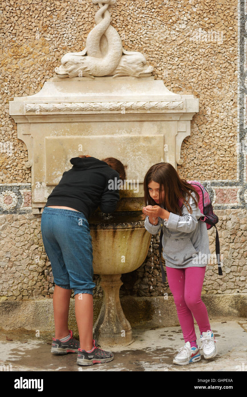 Portugal, Sintra, kids drinking water from a fountain at Quinta da Regaleira estate, a Unesco
