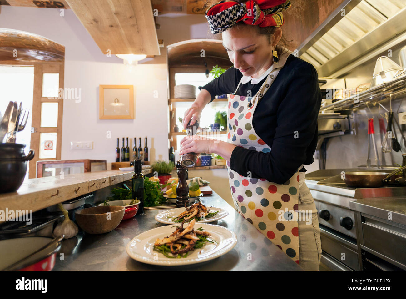 Female cook in restaurant seasoning food on plates Stock Photo