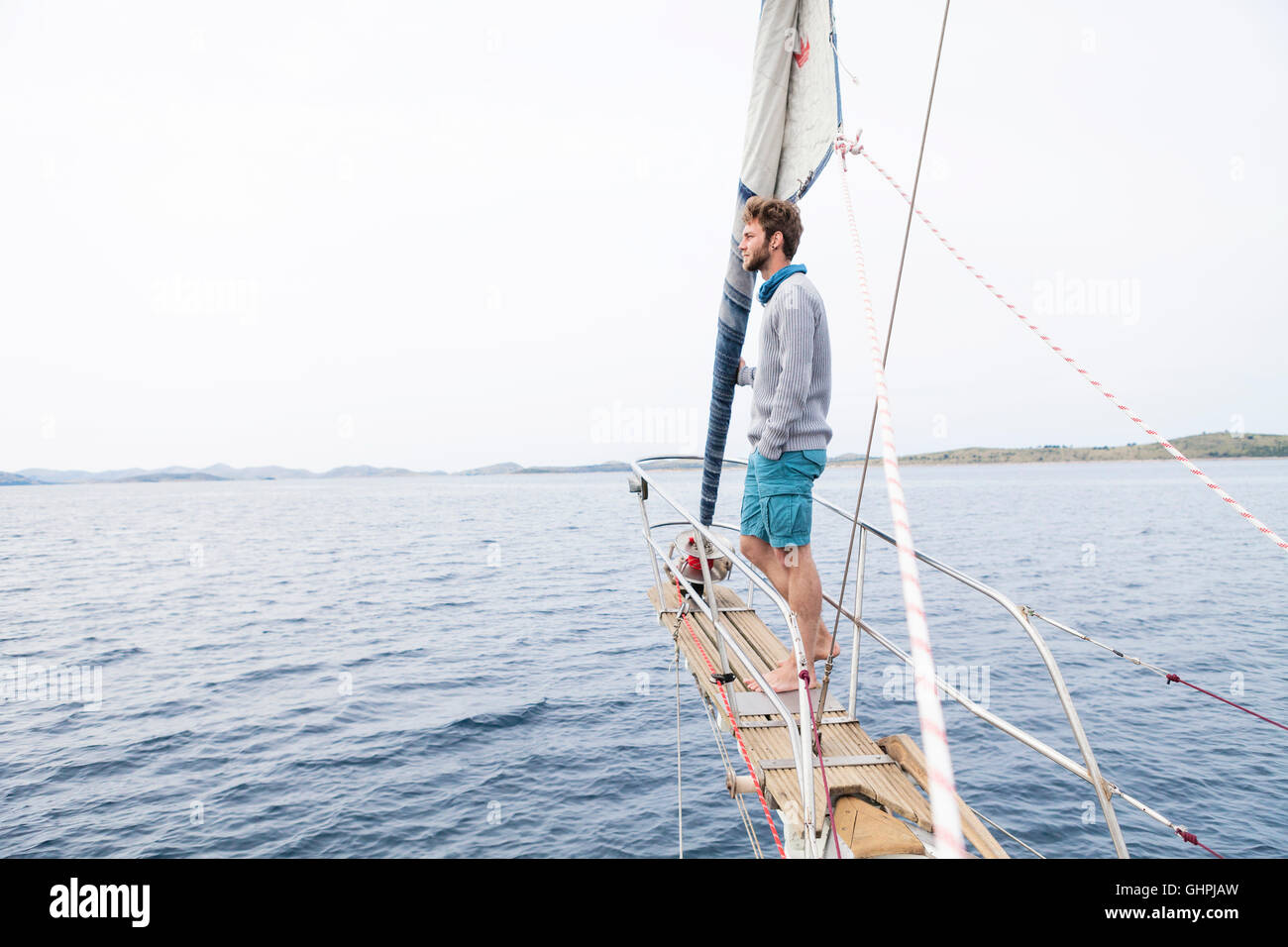 Young man stands on bow of yacht day dreaming Stock Photo