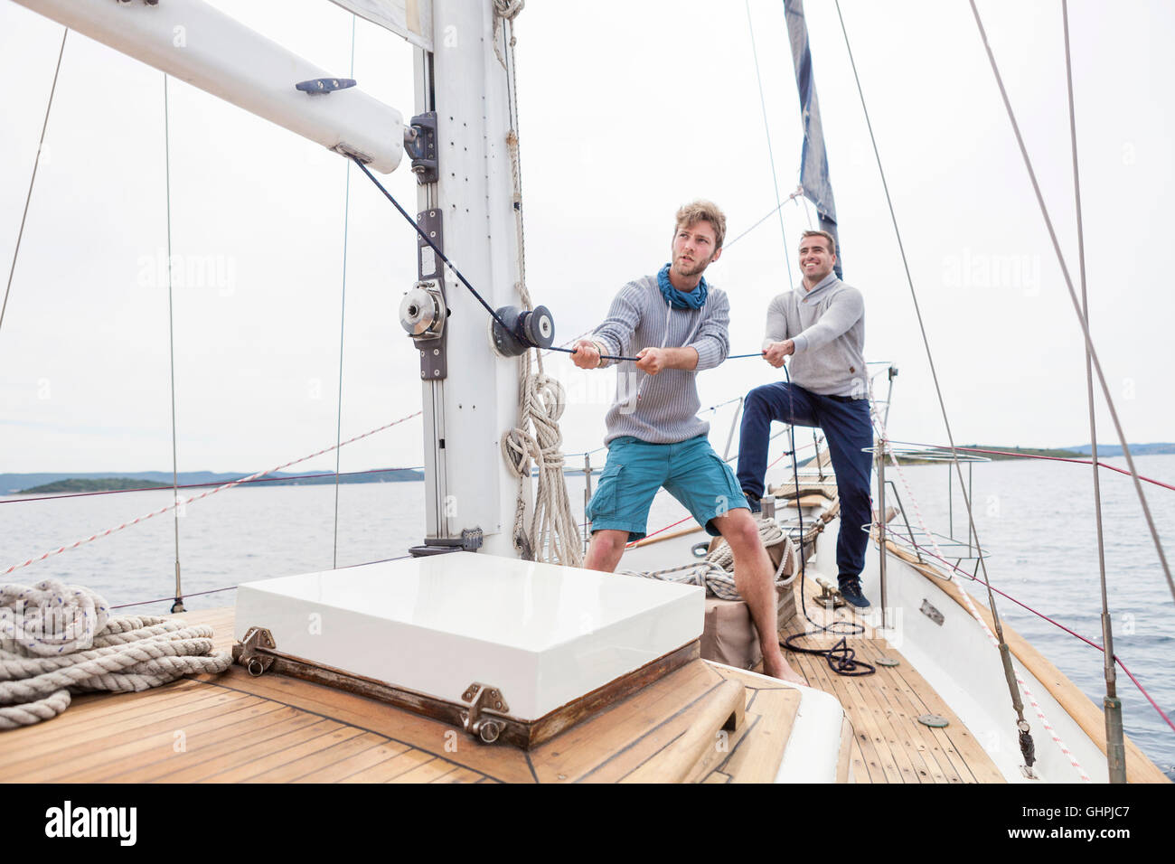 Two men pulling on rope on yacht Stock Photo