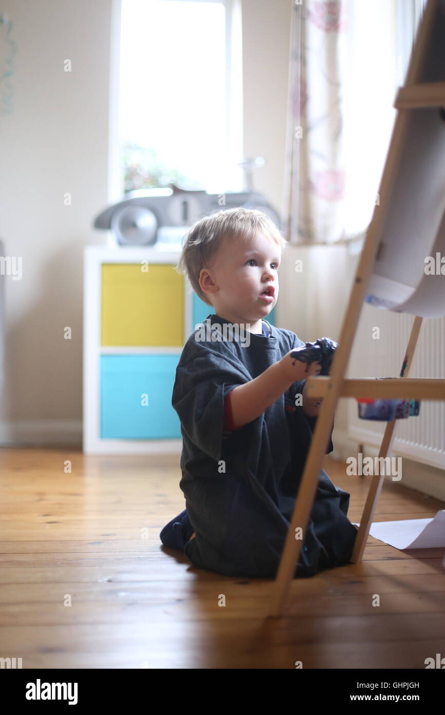 toddler boy painting in playroom on easel with car in background Stock
