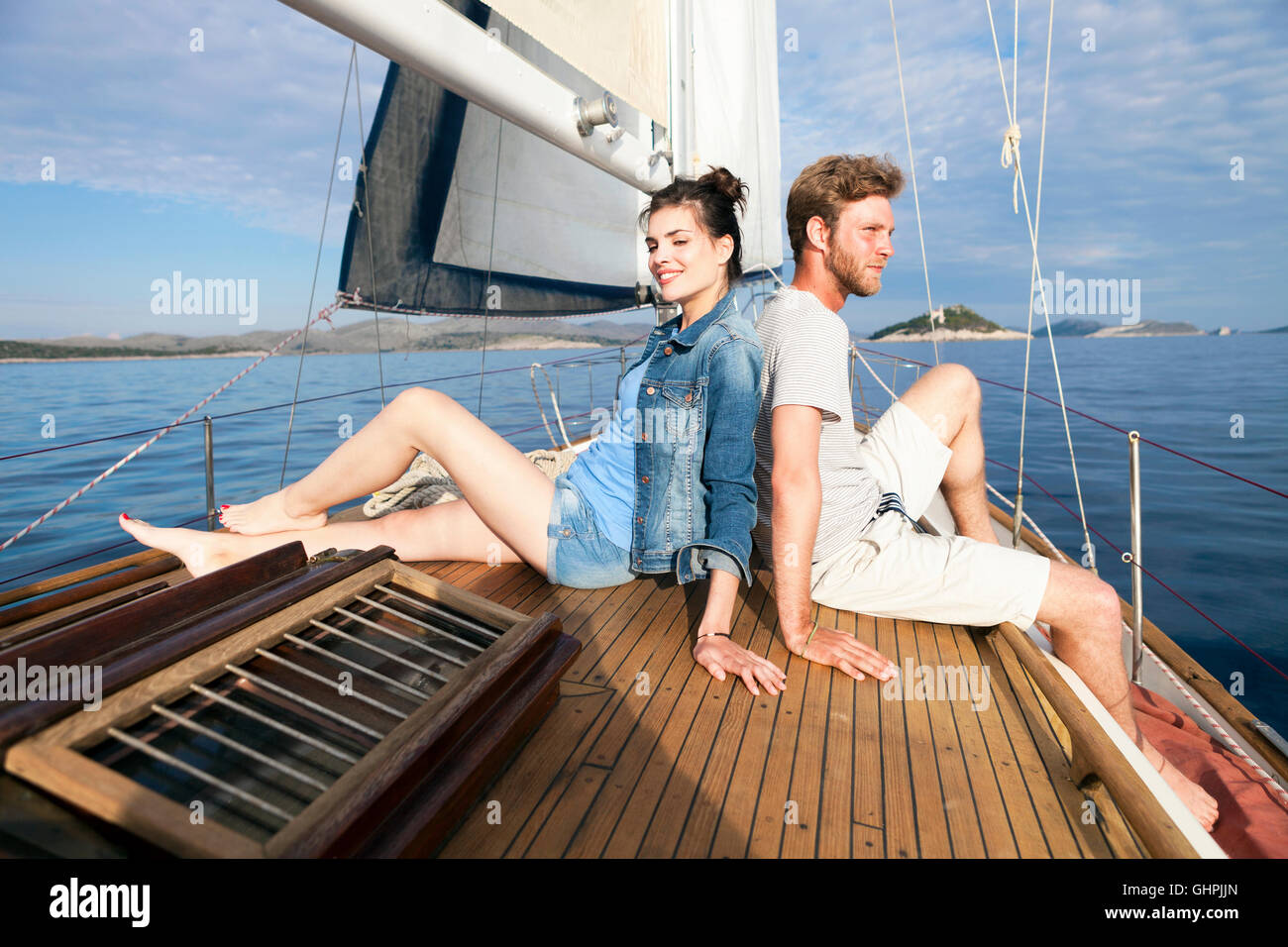 Young couple sitting back to back on sailboat Stock Photo