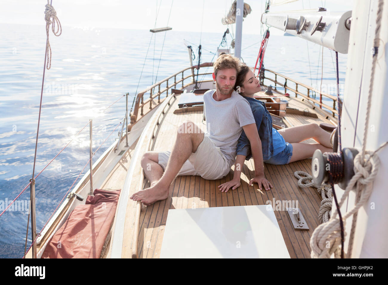 Young couple sitting back to back on sailboat Stock Photo