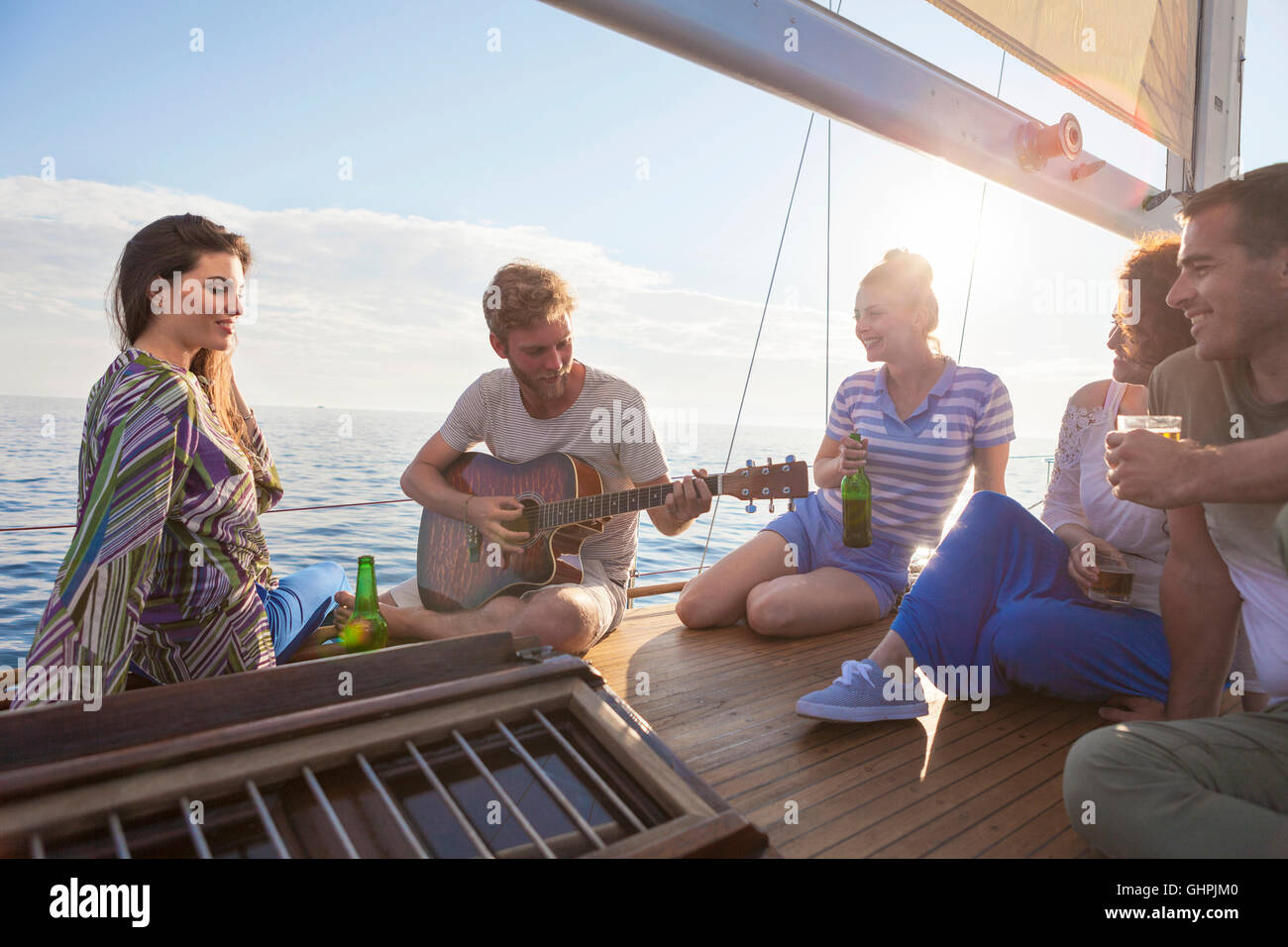 Young man playing guitar on sailboat with friends listening Stock Photo