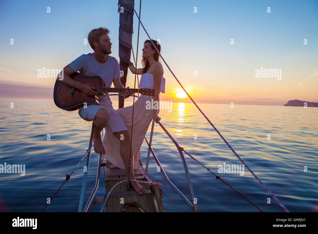 Young man playing guitar on sailboat at sunset Stock Photo