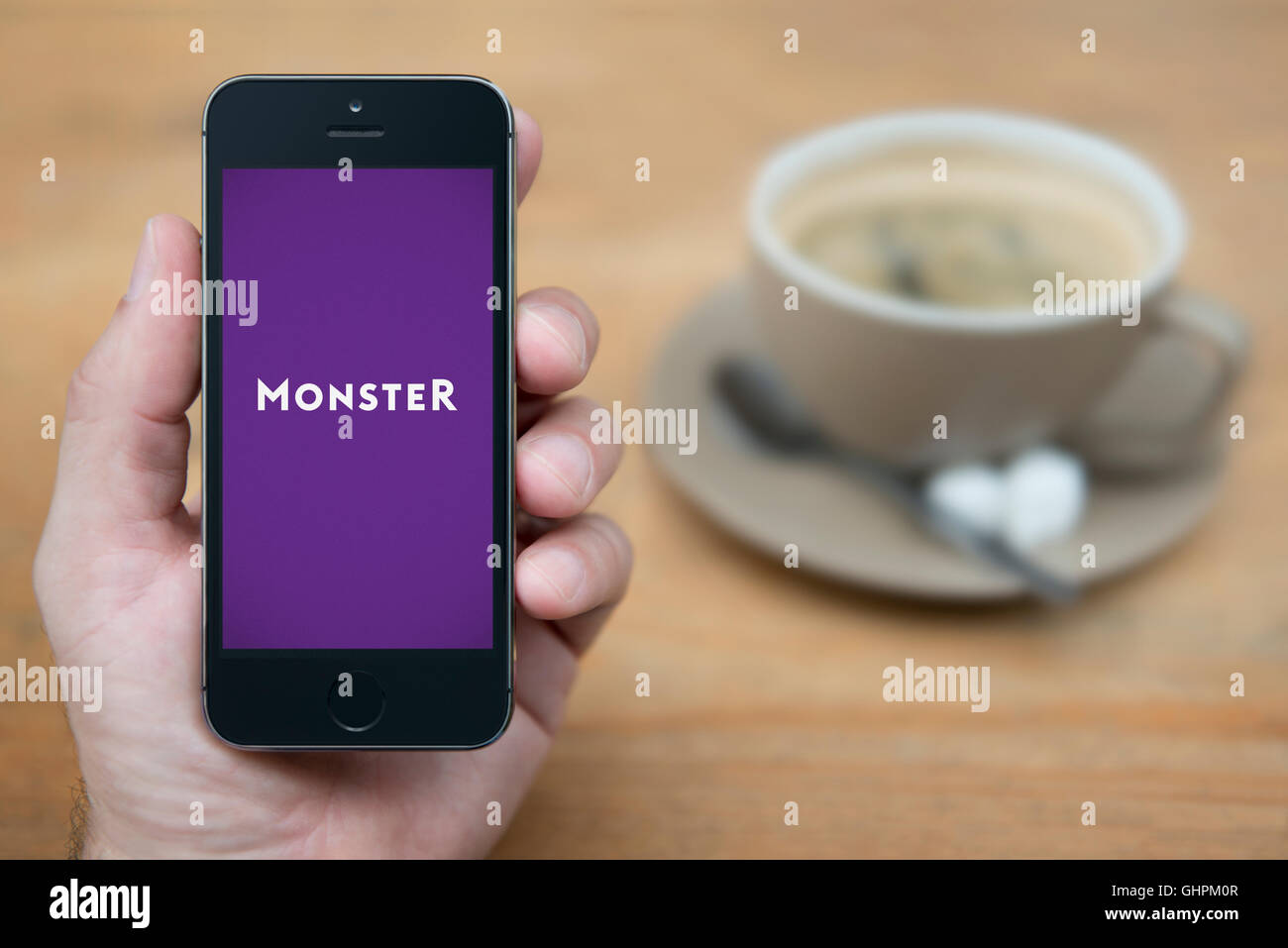 A man looks at his iPhone which displays the Monster logo, while sat with a cup of coffee (Editorial use only). Stock Photo
