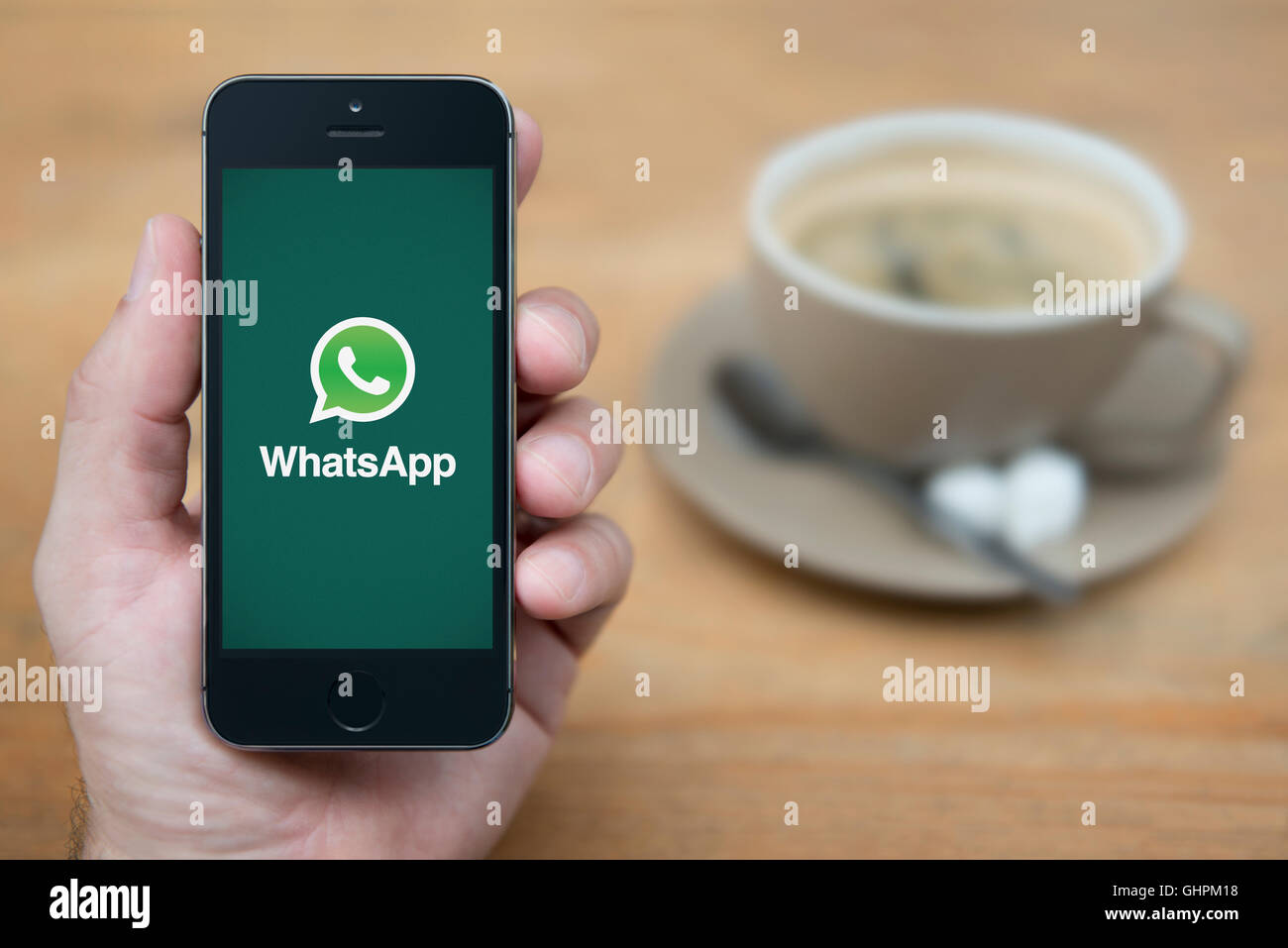 A man looks at his iPhone which displays the Whats App logo, while sat with a cup of coffee (Editorial use only). Stock Photo