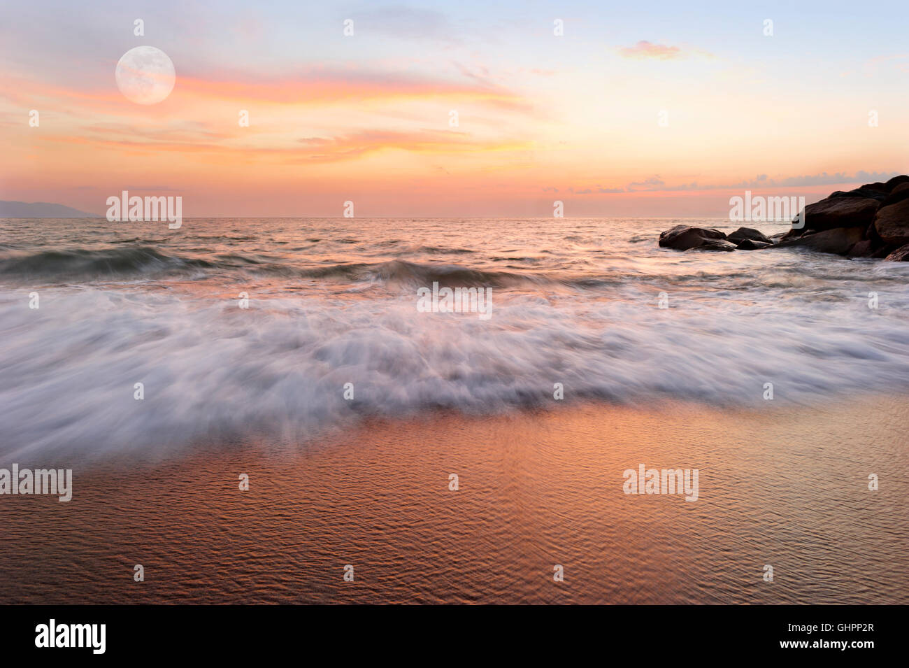 Ocean sunset is a soft pastel colored beach setting with a detailed cloudscape and a gentle wave rolling to shore. Stock Photo