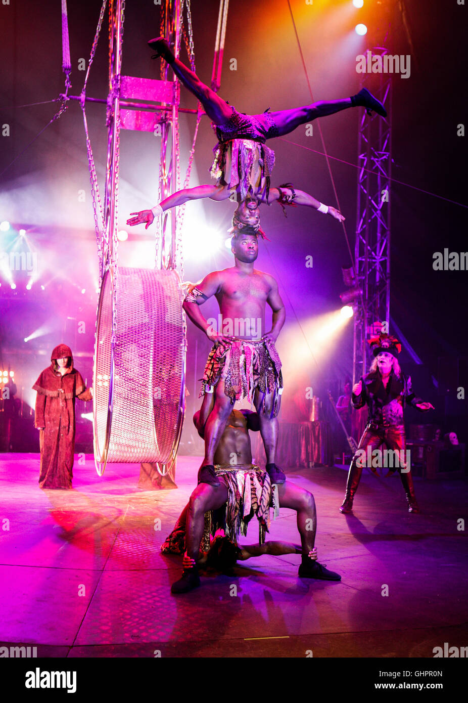 Circus of Horrors cast: The Kenyan Warriors acrobatic troupe in performance with ring master Dr Haze in the background on location in the big top. Stock Photo