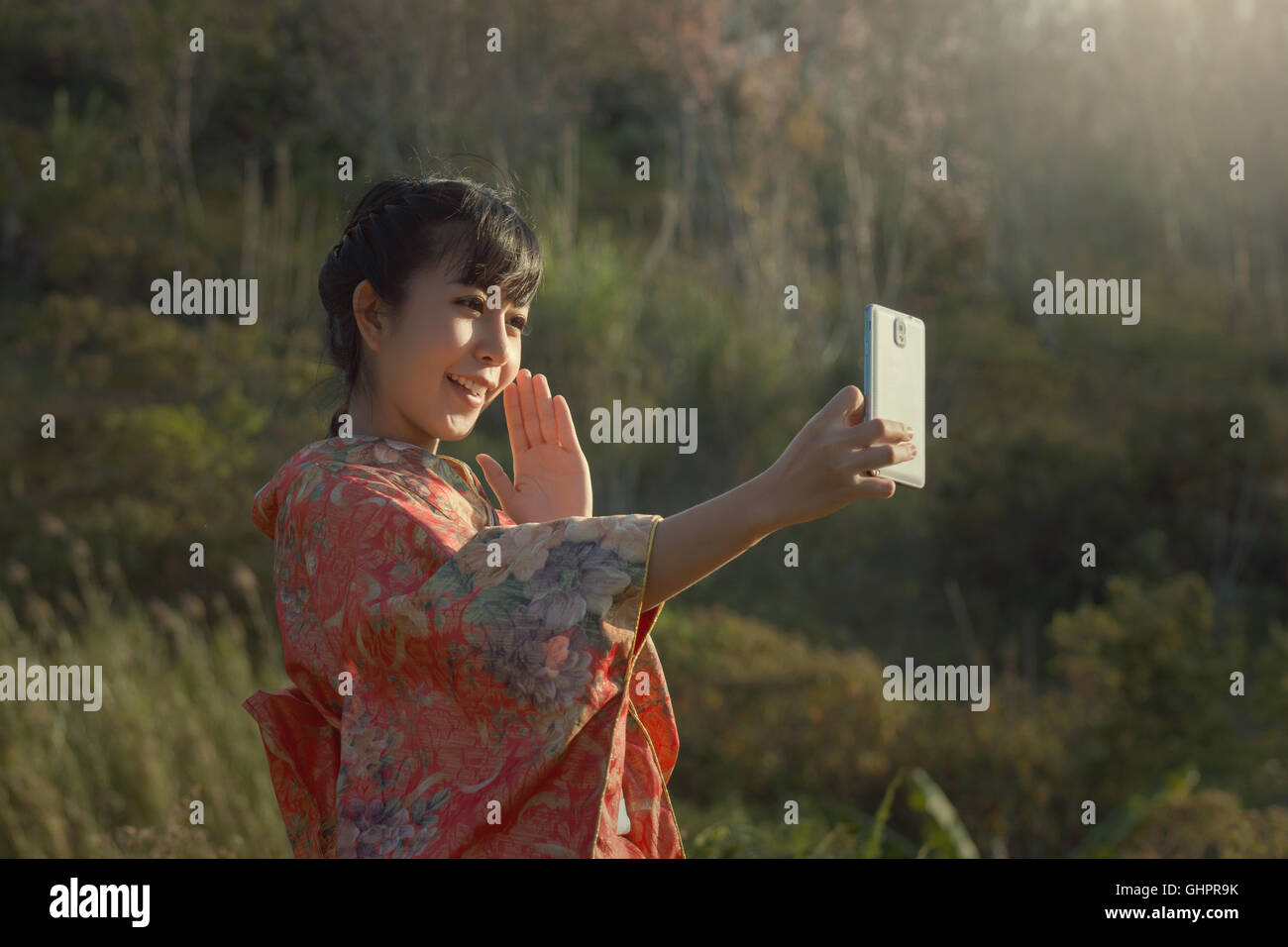 Beautiful smile selfie with smartphone in Kimono traditional japanese dress on the sakura garden. Stock Photo