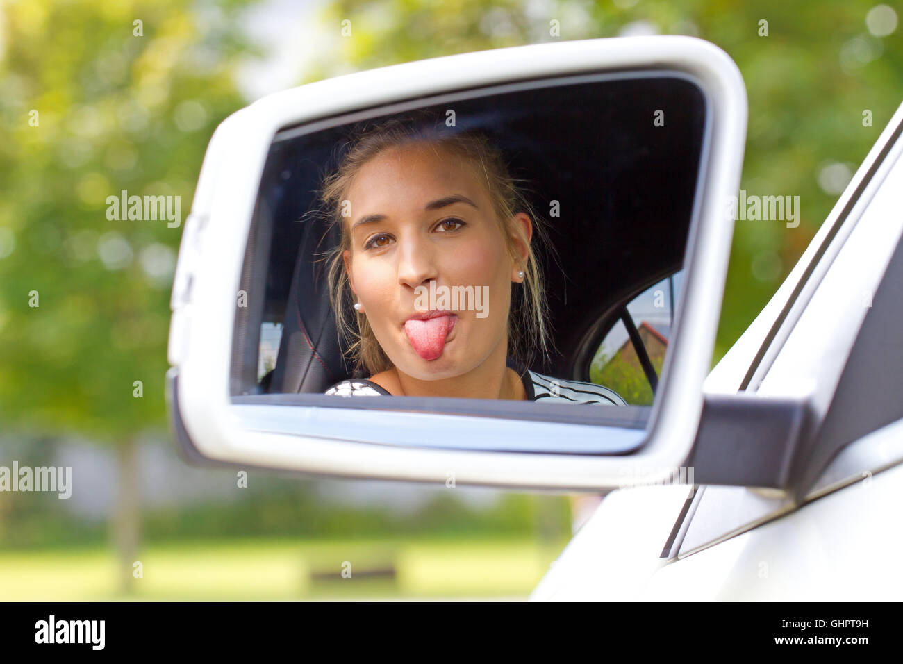 Young woman sticking tongue out in a car mirror Stock Photo