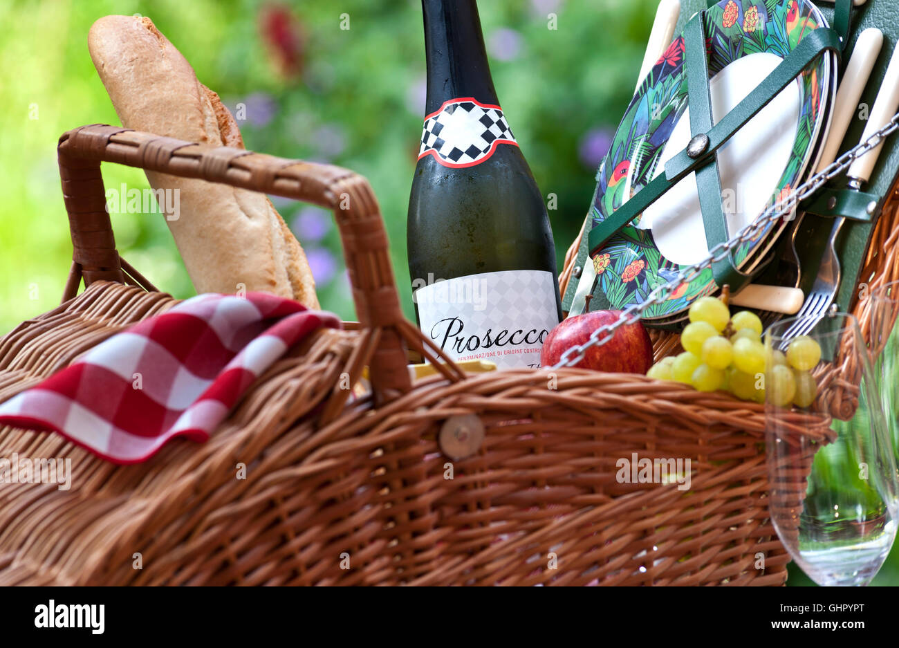 Prosecco wine bottle and wicker picnic basket in sunny floral garden situation Stock Photo