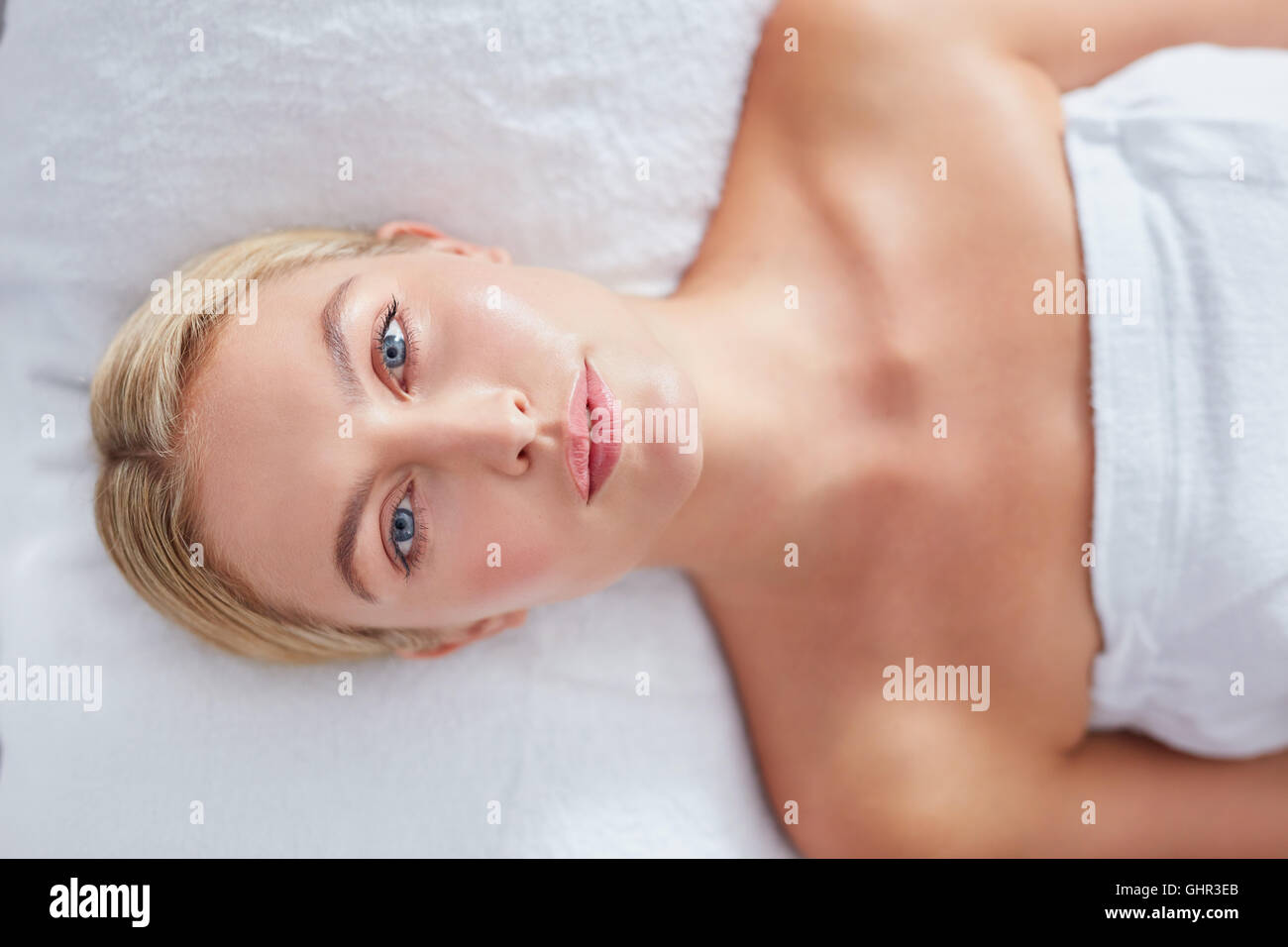 Top view of pretty young woman lying on massage table at dayspa. Woman with beautiful face and blue eyes. Stock Photo